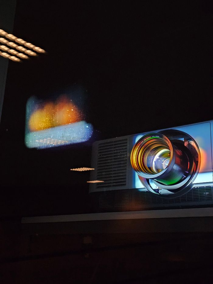 Projector lens reflecting colorful light pattern onto a dark wall.